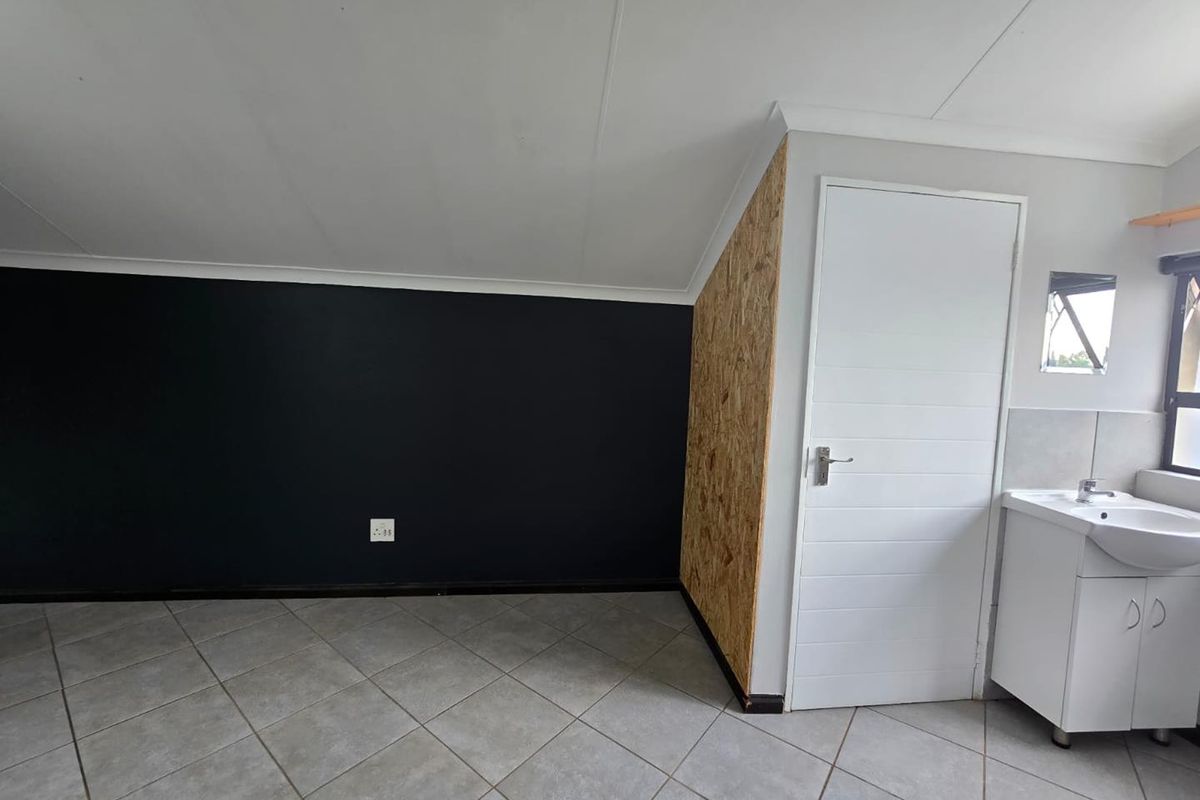 A functional room featuring tiled flooring, a built-in vanity basin, and a unique combination of dark accent walls and exposed OSB paneling.