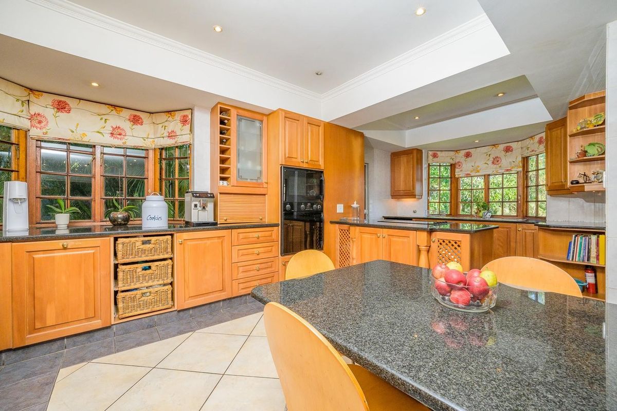 Spacious kitchen featuring timber cabinetry, granite countertops, built-in appliances, and ample natural light from large bay windows.