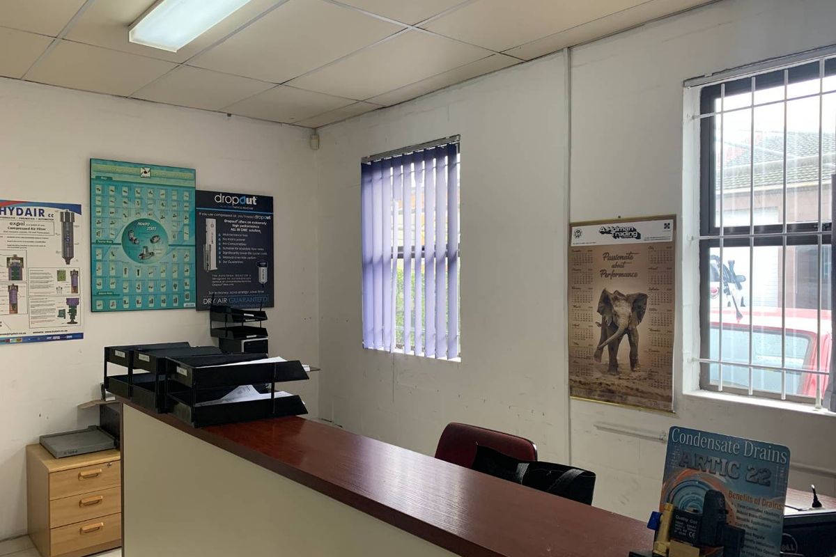 A functional office space featuring a built-in reception counter, security bars on windows, and a suspended ceiling with integrated lighting.