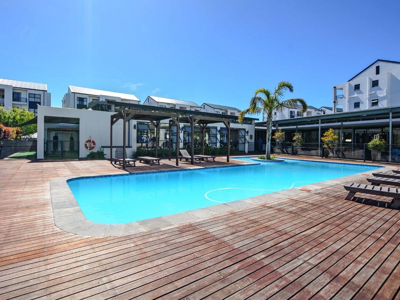 Communal swimming pool area featuring extensive timber decking, a timber pergola structure, and modern apartment building surrounds.