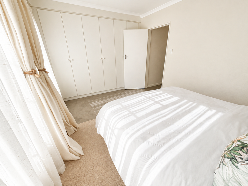A bright and airy bedroom featuring neutral tones, ample built-in cupboard storage, and soft carpeted flooring, creating a comfortable and inviting living space.