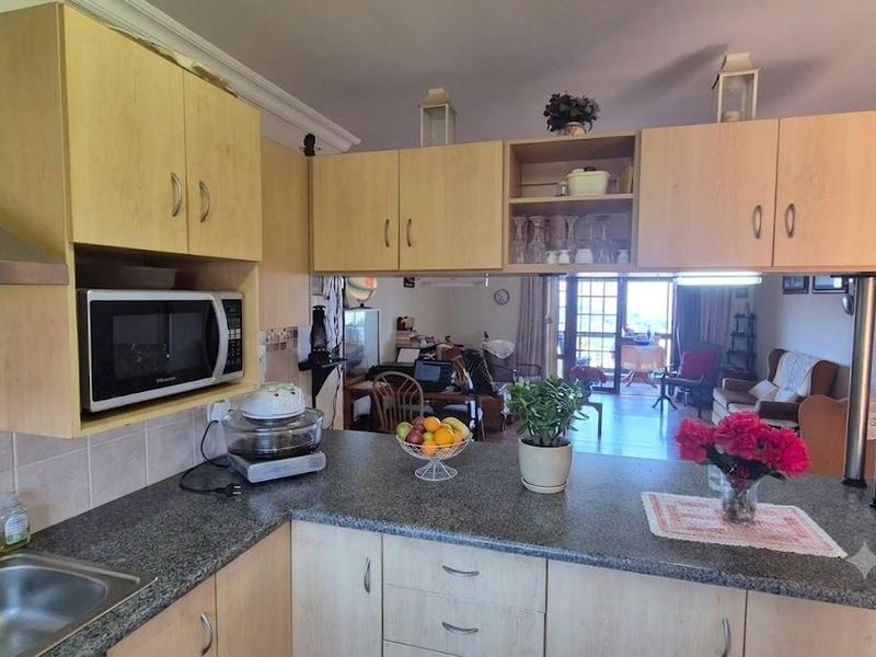 Open-plan kitchen featuring light wood laminate cabinetry, granite countertops, and a breakfast bar overlooking the living area and balcony.