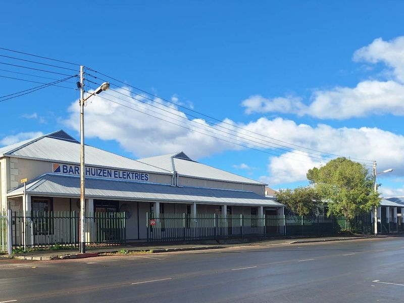 Street-level view of an industrial property featuring a corrugated metal roof, a covered veranda, and secure perimeter fencing.
