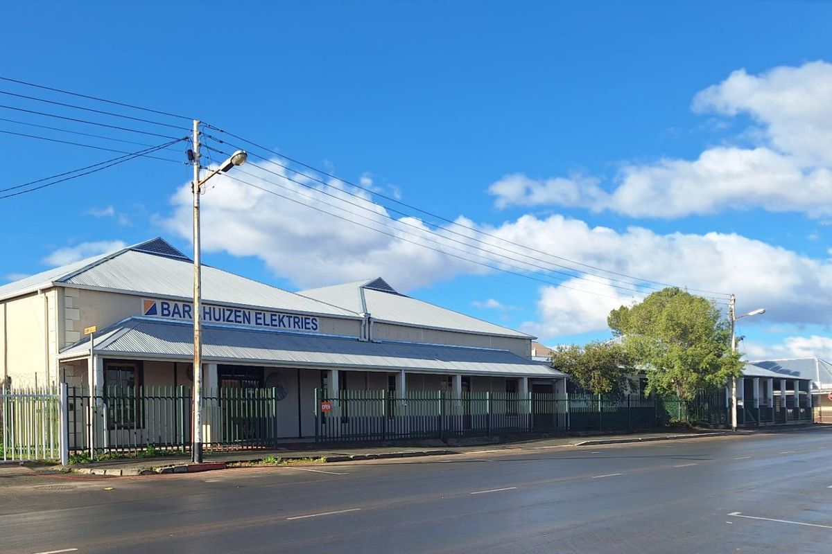 Street-level view of an industrial property featuring a corrugated metal roof, a covered veranda, and secure perimeter fencing.