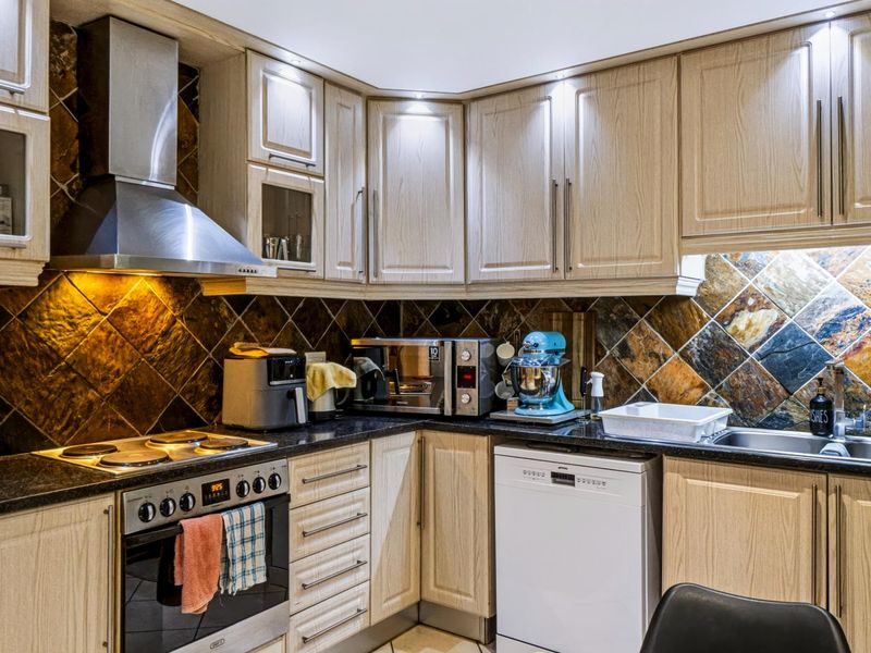 A well-maintained kitchen featuring light wood cabinetry, dark stone countertops, a decorative stone tile backsplash, and built-in stainless steel appliances.