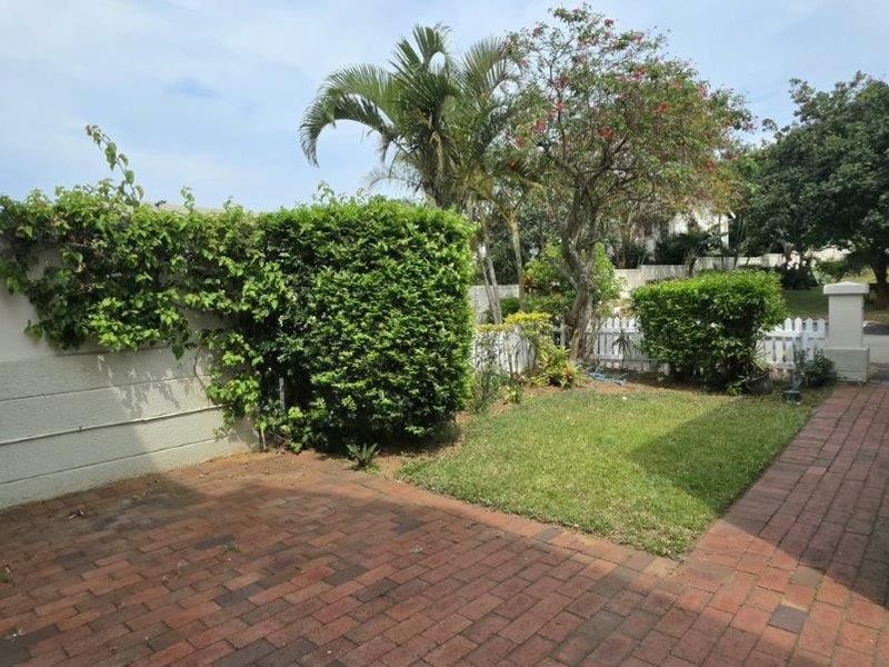 A private rear courtyard featuring brick paving, a small lawn, and established garden borders enclosed by a boundary wall and picket fencing.