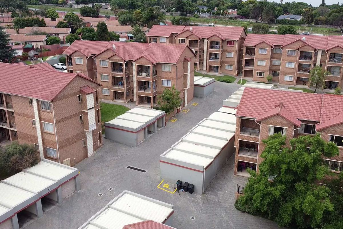 Aerial view of a residential apartment complex featuring multiple brick buildings with tiled roofs, paved driveways, and dedicated carport parking areas.