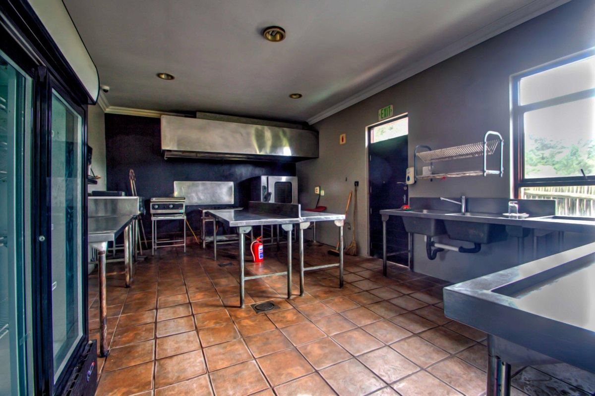 Commercial-grade kitchen featuring stainless steel prep tables, industrial extractor hood, double basin sink, and tiled flooring suitable for high-volume food preparation.