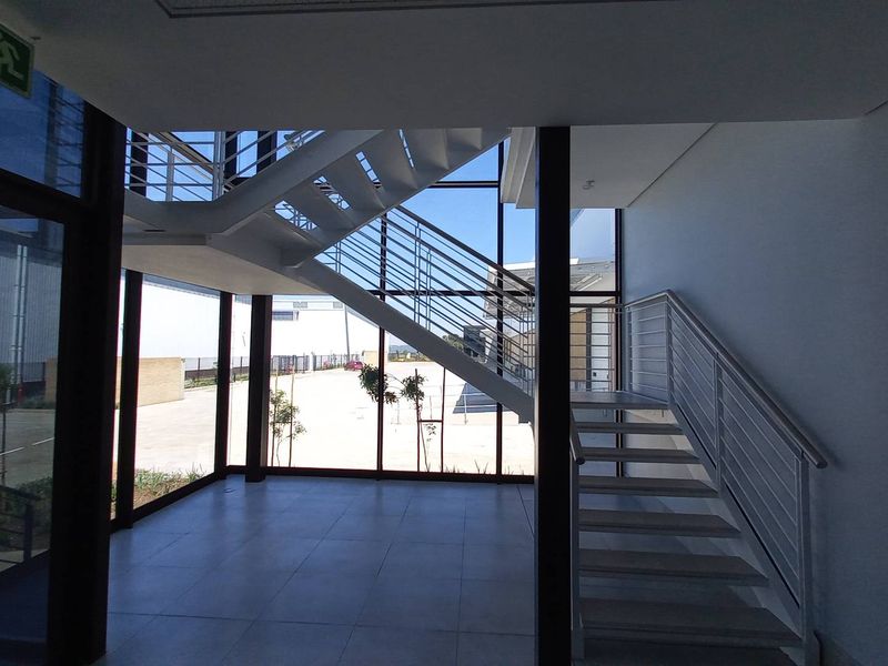 Modern industrial entrance foyer featuring a sleek metal staircase, expansive floor-to-ceiling glass windows, and clean tiled flooring in a bright, open-plan setting.