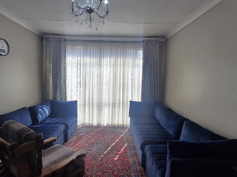 A comfortable living room featuring neutral walls, coving, and large windows dressed with floor-to-ceiling curtains, providing a bright and inviting space.