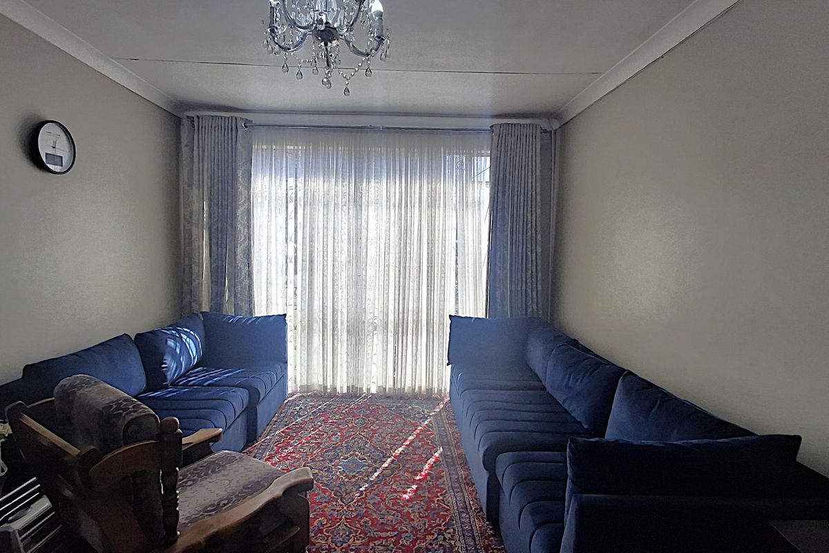 A comfortable living room featuring neutral walls, coving, and large windows dressed with floor-to-ceiling curtains, providing a bright and inviting space.