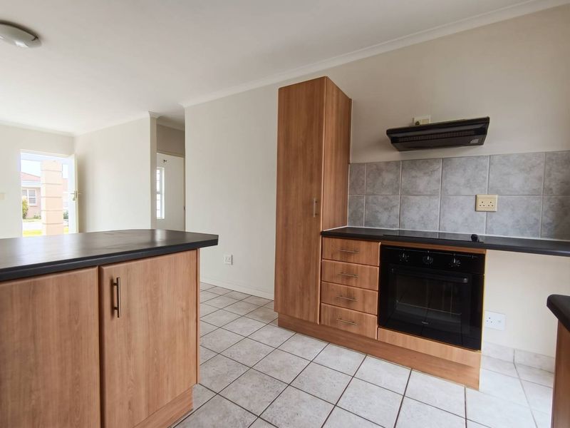 A clean, functional kitchen featuring wood-look cabinetry, built-in oven, extractor fan, tiled flooring, and a neutral tiled backsplash.