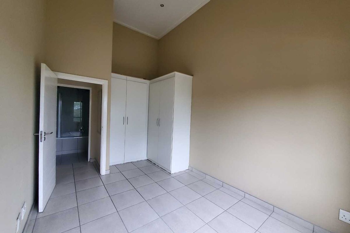 A bright, empty bedroom featuring neutral tiled flooring, built-in white wardrobes, and direct access to an en-suite bathroom.