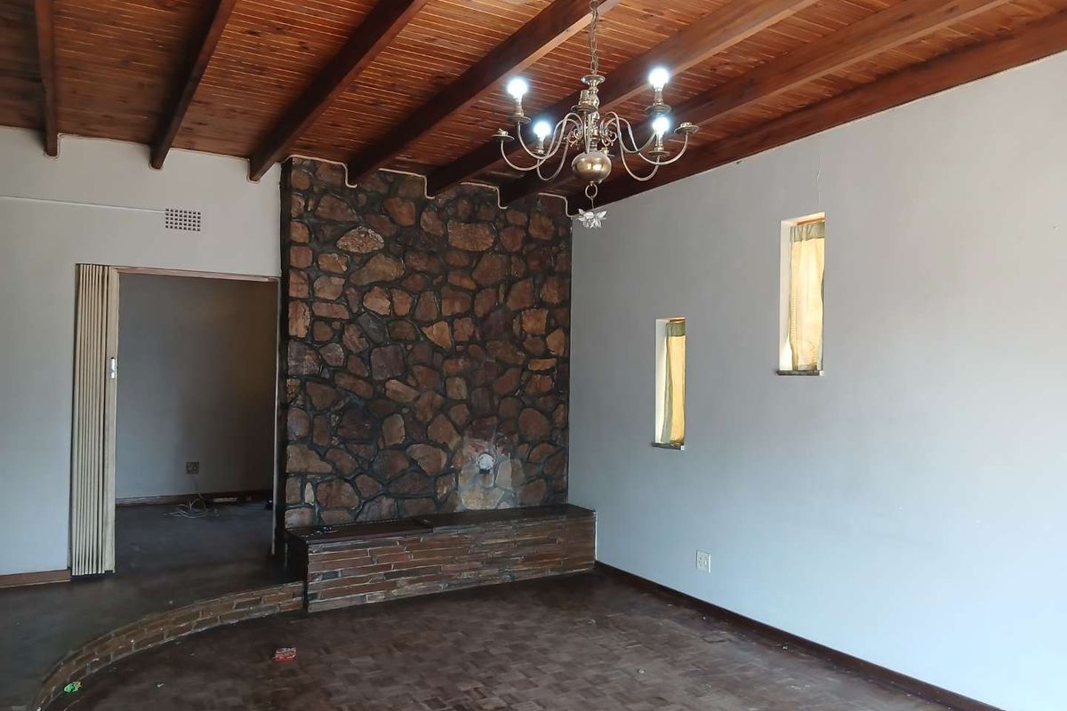 Spacious living room featuring a rustic stone fireplace, exposed timber beam ceiling, and classic parquet flooring, offering a character-filled blank canvas.