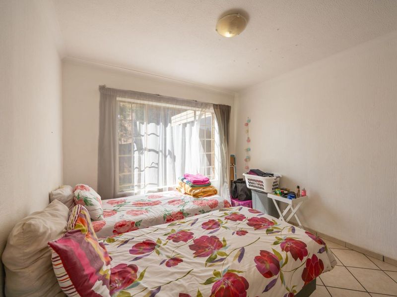 A bedroom featuring tiled flooring, a central ceiling light, and a window with curtain tracks, providing a functional space for rest.