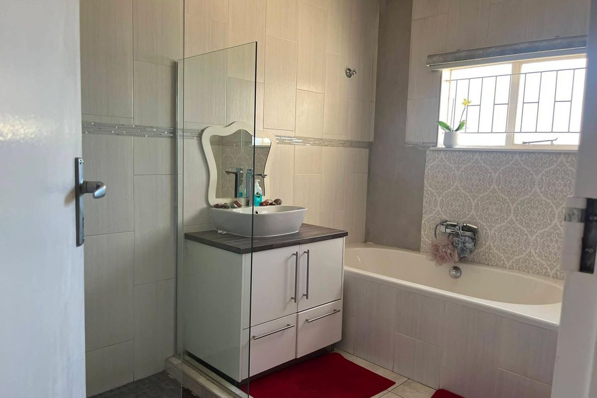 A functional bathroom featuring a vanity with a vessel sink, a bathtub, and a glass shower screen with neutral wall tiling.