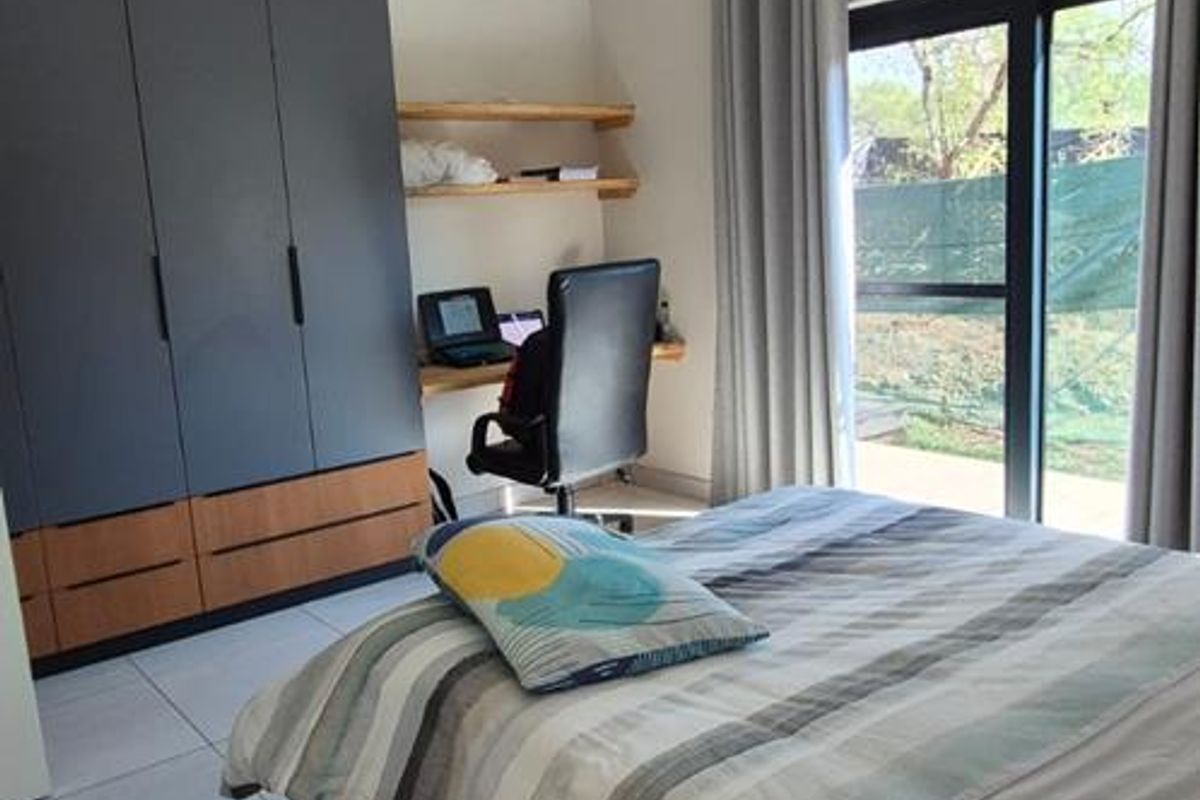 A well-lit bedroom featuring tiled flooring, a built-in wardrobe, a ceiling fan, and sliding glass doors providing access to the exterior.