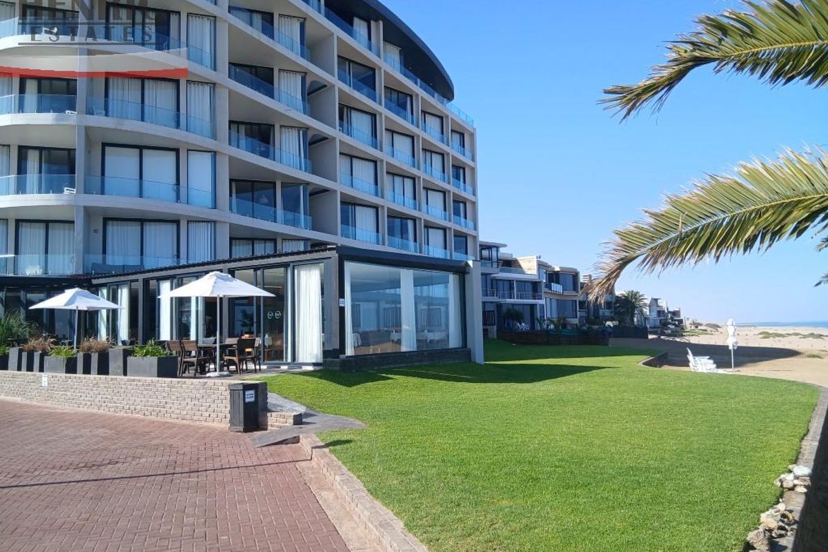 A view of the rear apartment facade featuring modern glass balconies, a well-maintained lawn, and direct access to the coastal area.