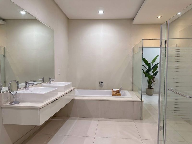 Modern bathroom featuring a double vanity with vessel sinks, a built-in bathtub, and a separate glass-enclosed shower area with neutral tile finishes.
