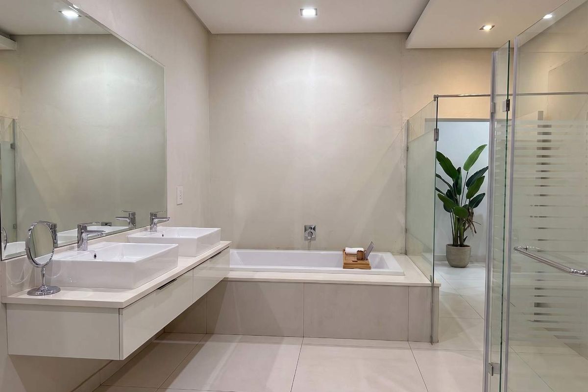 Modern bathroom featuring a double vanity with vessel sinks, a built-in bathtub, and a separate glass-enclosed shower area with neutral tile finishes.