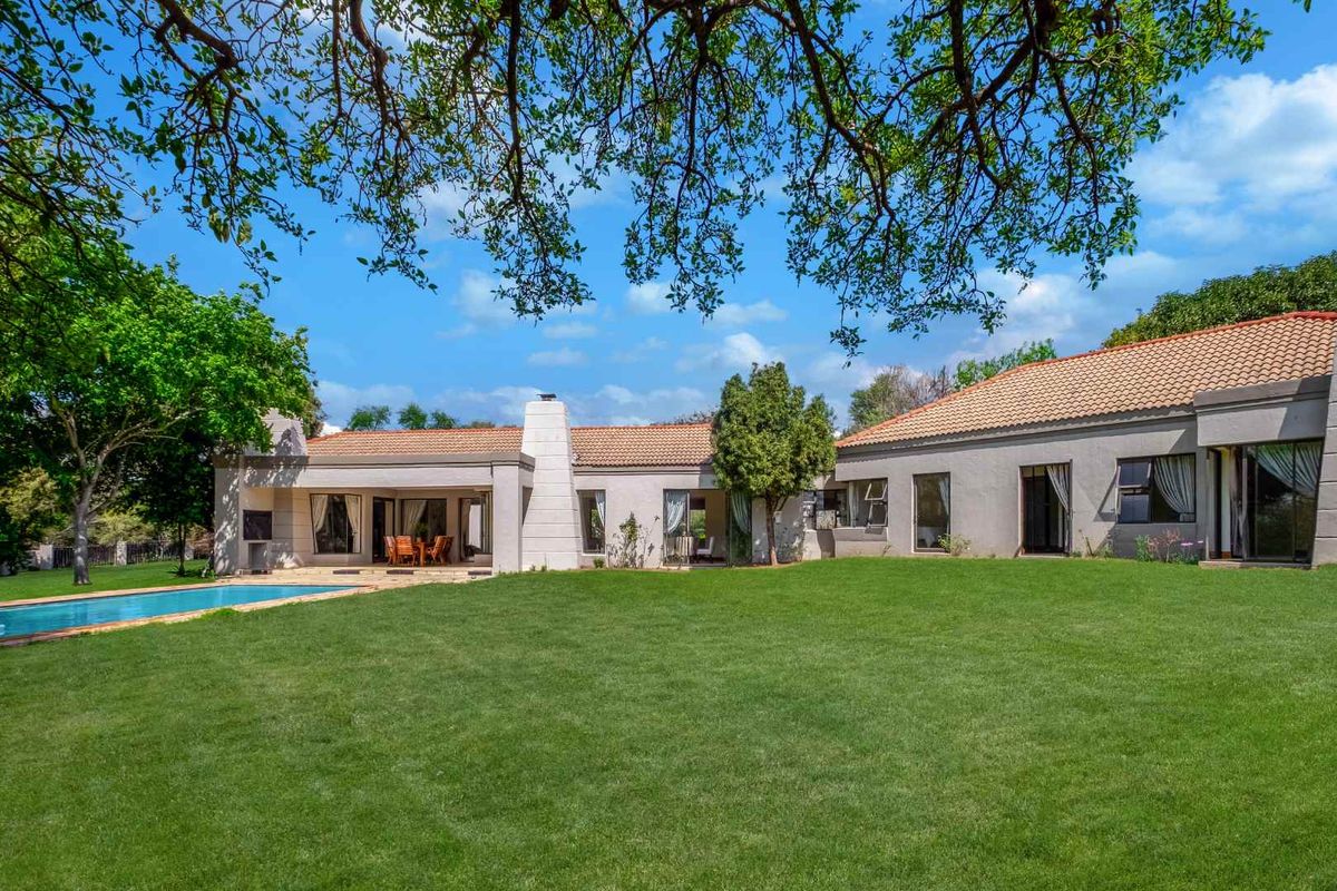 Spacious rear garden featuring a well-maintained lawn, swimming pool, and a single-story residence with terracotta roof tiles and multiple access points.