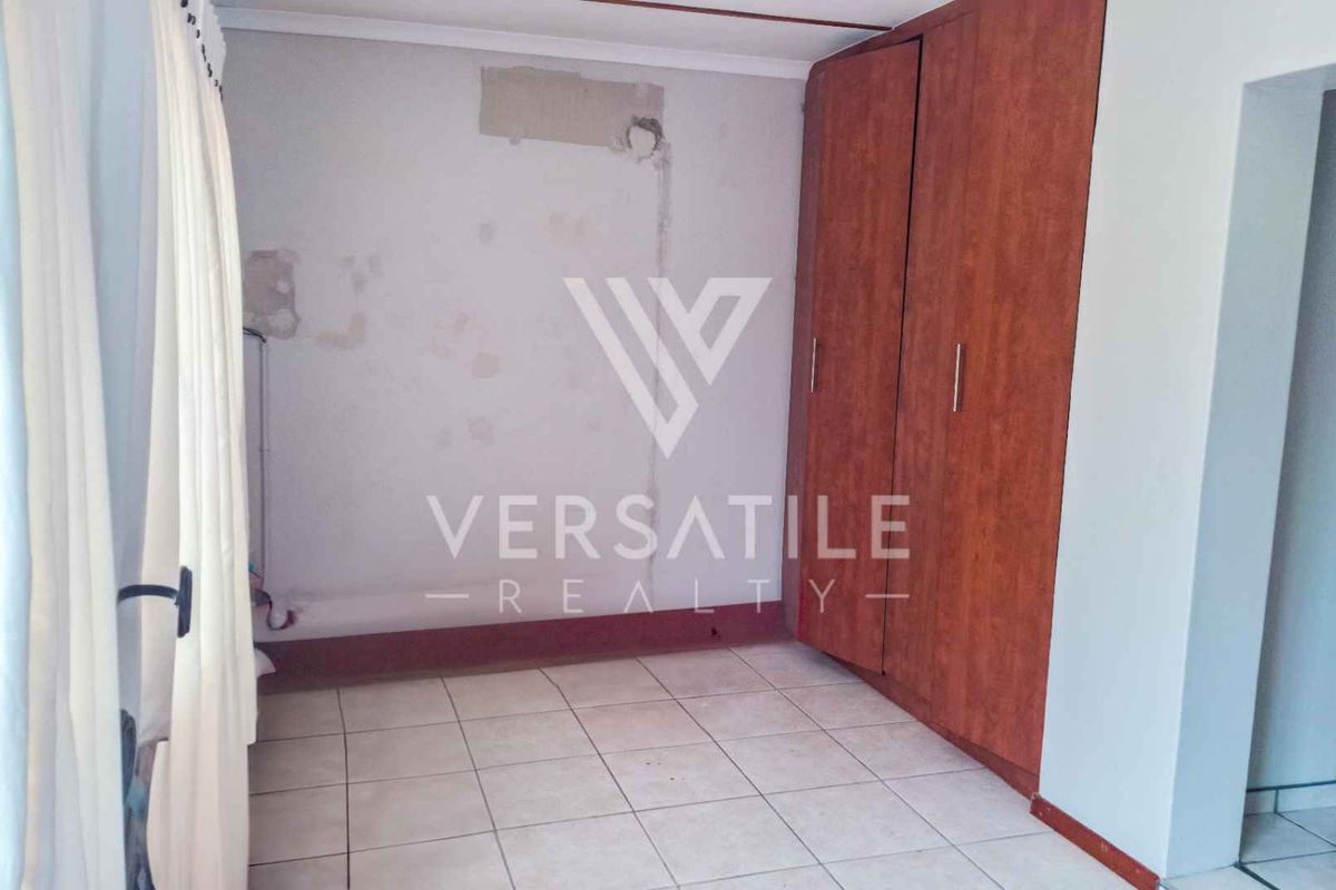 A bedroom featuring built-in wooden cupboards and tiled flooring, currently showing signs of wall surface damage and exposed electrical points.