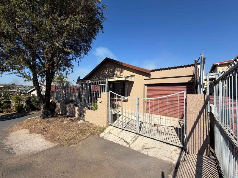 Front exterior view of a single-story house featuring a metal security gate, perimeter wall, and attached garage with a tiled roof.