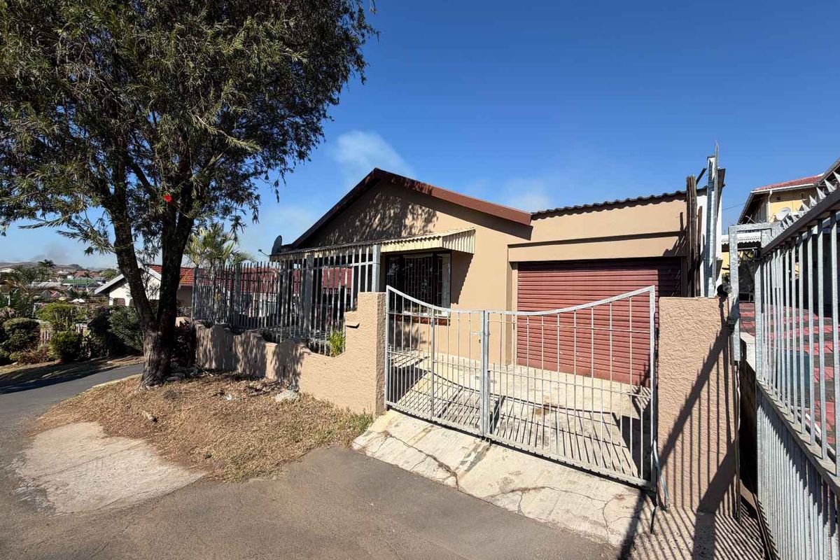 Front exterior view of a single-story house featuring a metal security gate, perimeter wall, and attached garage with a tiled roof.