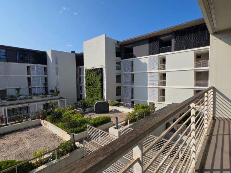 View from a balcony overlooking a modern apartment complex courtyard featuring a vertical garden, paved areas, and architectural louvre shutters.