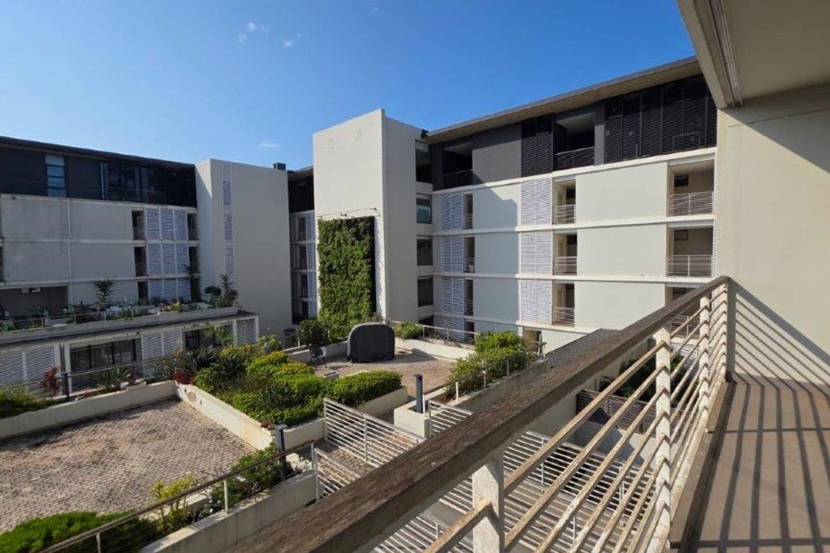 View from a balcony overlooking a modern apartment complex courtyard featuring a vertical garden, paved areas, and architectural louvre shutters.
