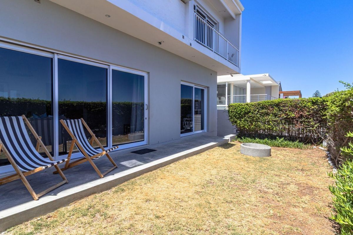 Rear exterior view featuring a concrete patio, sliding glass doors, and a small private garden area with established hedging.