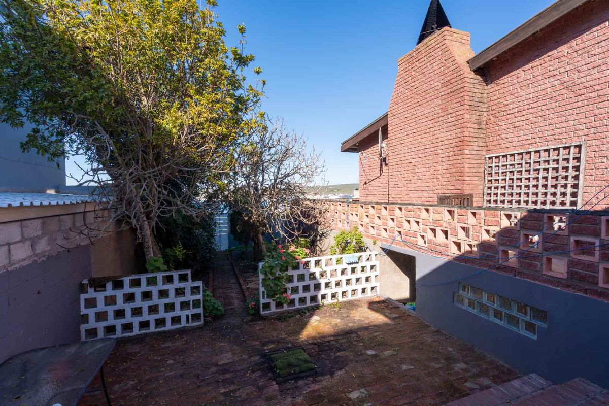 A rear garden area featuring a brick chimney, decorative breeze block walls, and brick paving, showing signs of age and weathering.