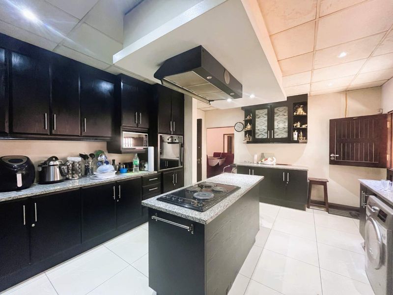 Spacious kitchen featuring dark cabinetry, granite countertops, a central island with a built-in hob, and an integrated extractor fan.