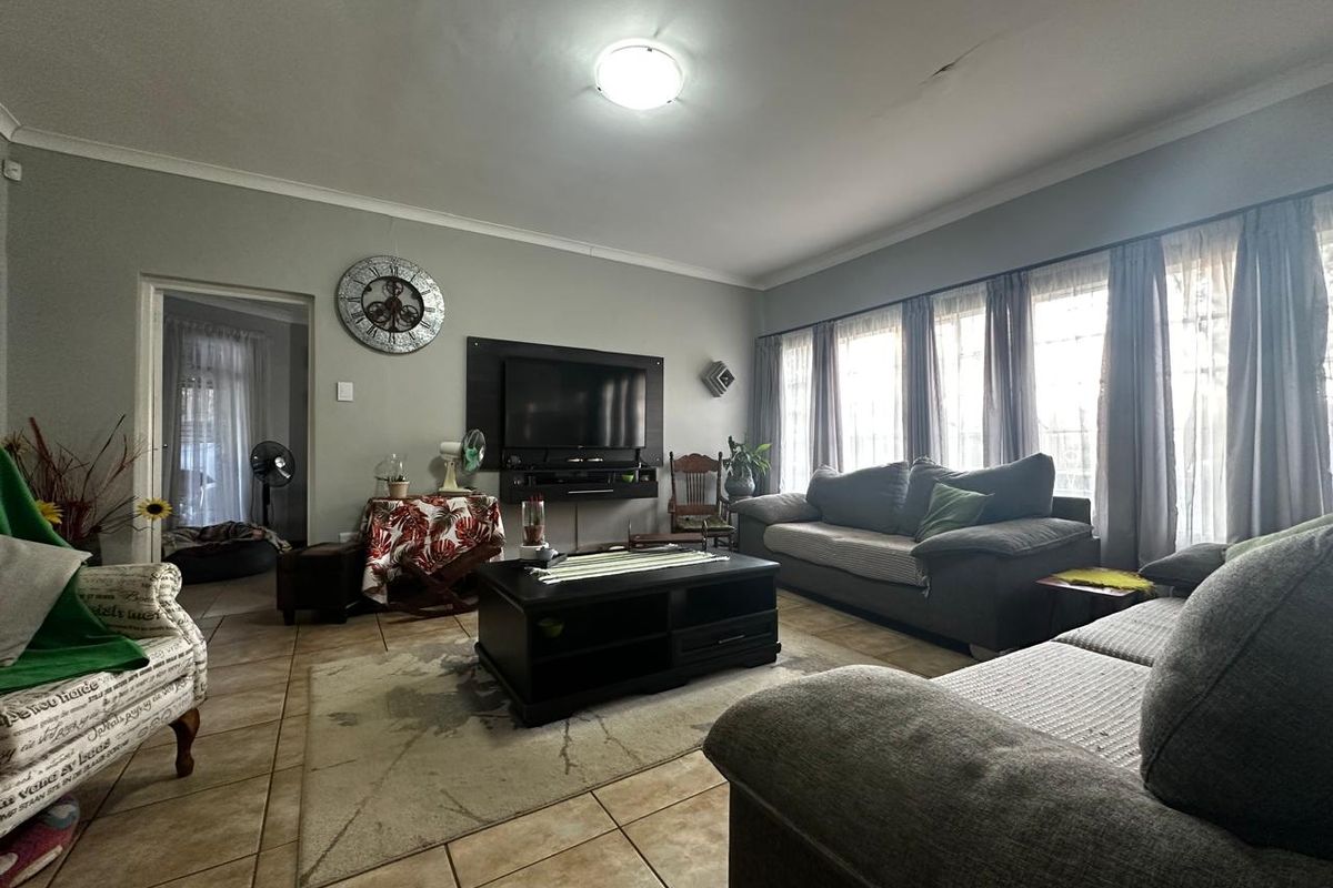 A spacious living room featuring tiled flooring, large windows with natural light, and a dedicated wall-mounted television area.