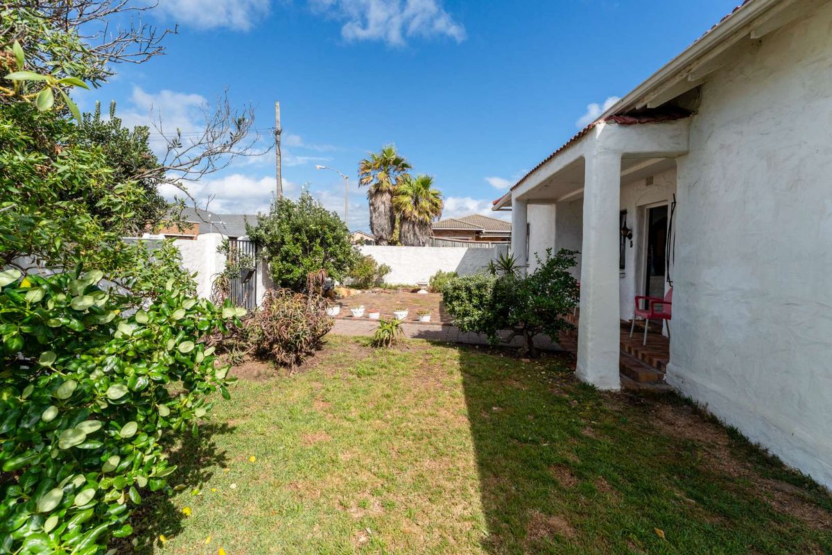 A rear garden view featuring a covered patio area, lawn, and perimeter boundary walls.