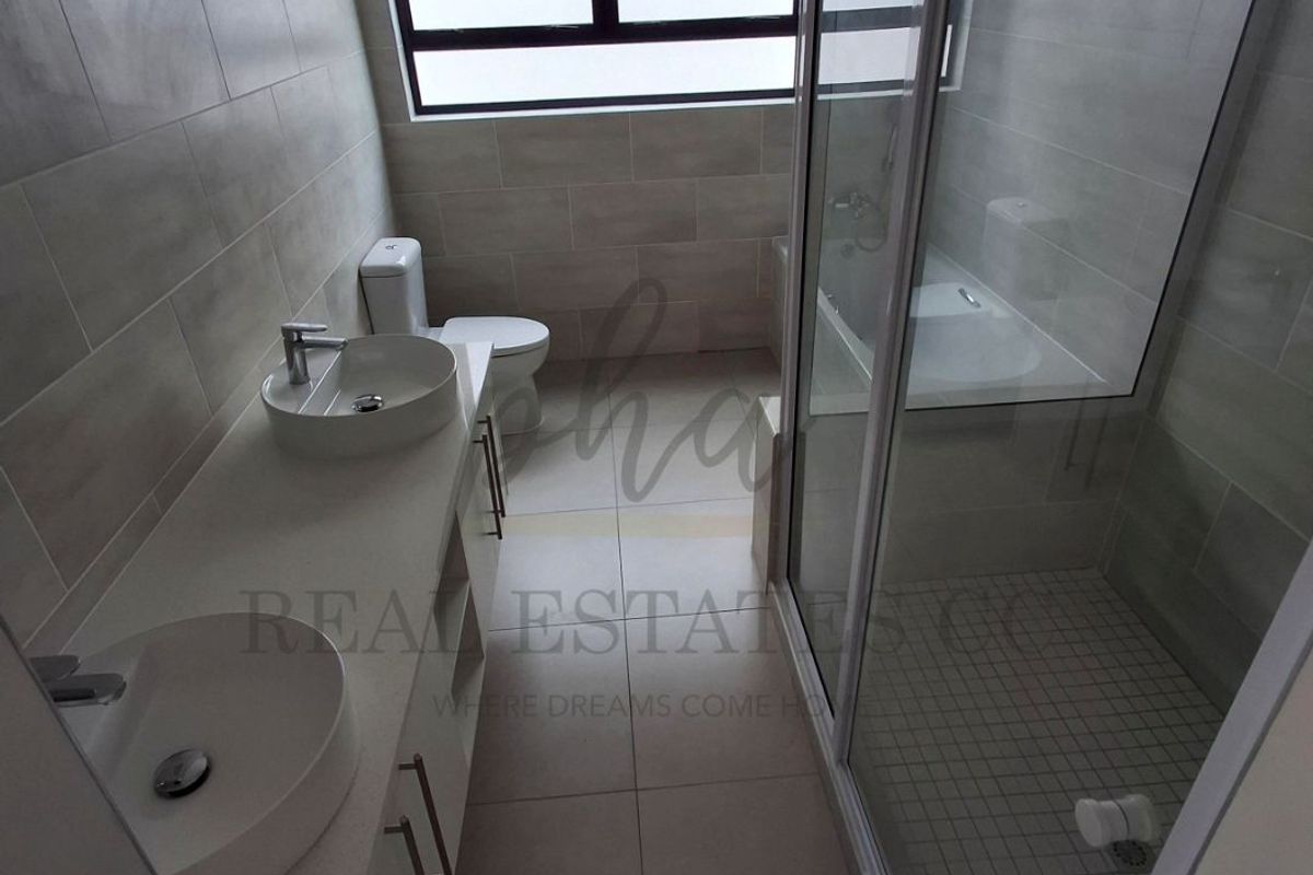 Modern bathroom featuring a double vanity with vessel sinks, a glass-enclosed shower, and neutral floor-to-ceiling tiling.