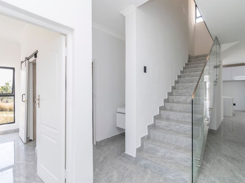 Modern entrance hallway featuring a sleek glass balustrade staircase, high-quality porcelain floor tiles, and a contemporary sliding barn door.