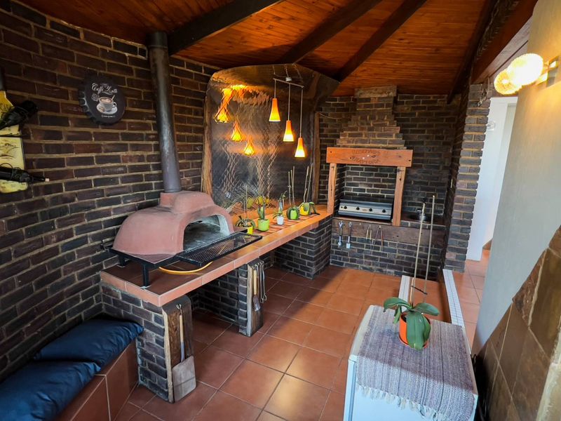 Covered outdoor entertainment area featuring a built-in brick braai, pizza oven, tiled flooring, and exposed timber beam ceiling.