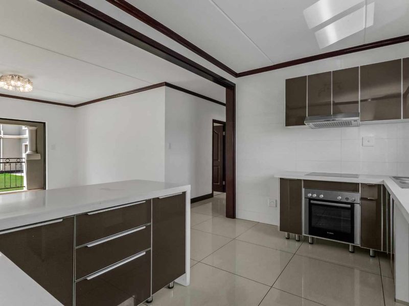 Modern open-plan kitchen featuring sleek brown cabinetry, integrated appliances, and tiled flooring, seamlessly flowing into the living area with access to a private balcony.