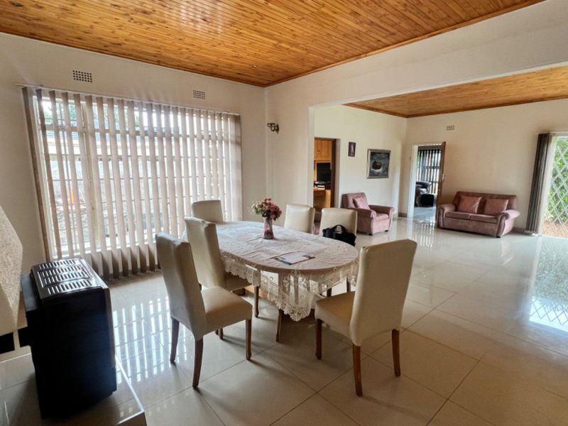 Spacious open-plan living and dining area featuring tiled floors, a warm timber ceiling, and large sliding doors providing natural light and garden access.
