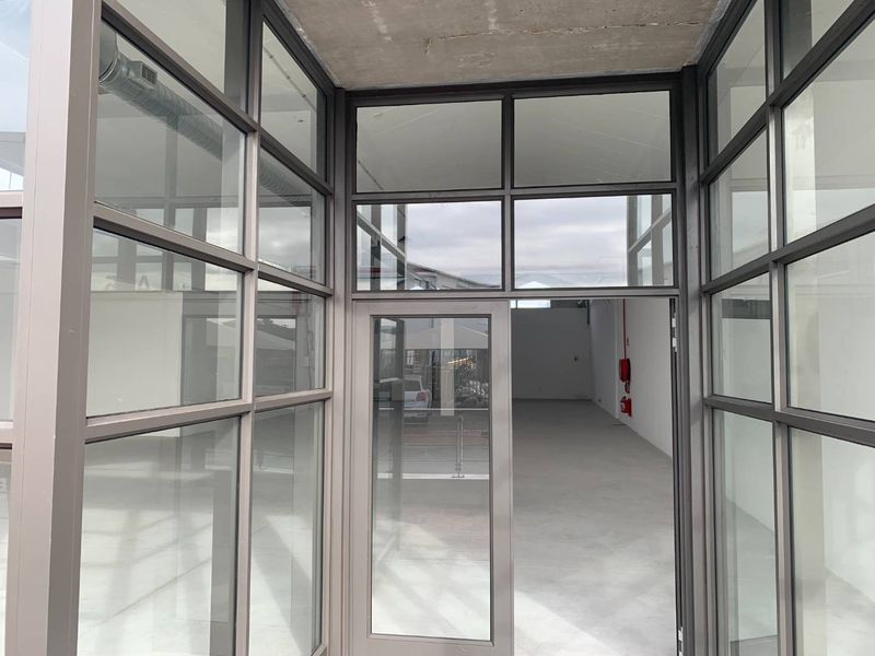 A modern, vacant retail entrance featuring extensive aluminium-framed glass partitioning, polished concrete floors, and an exposed industrial-style ceiling.