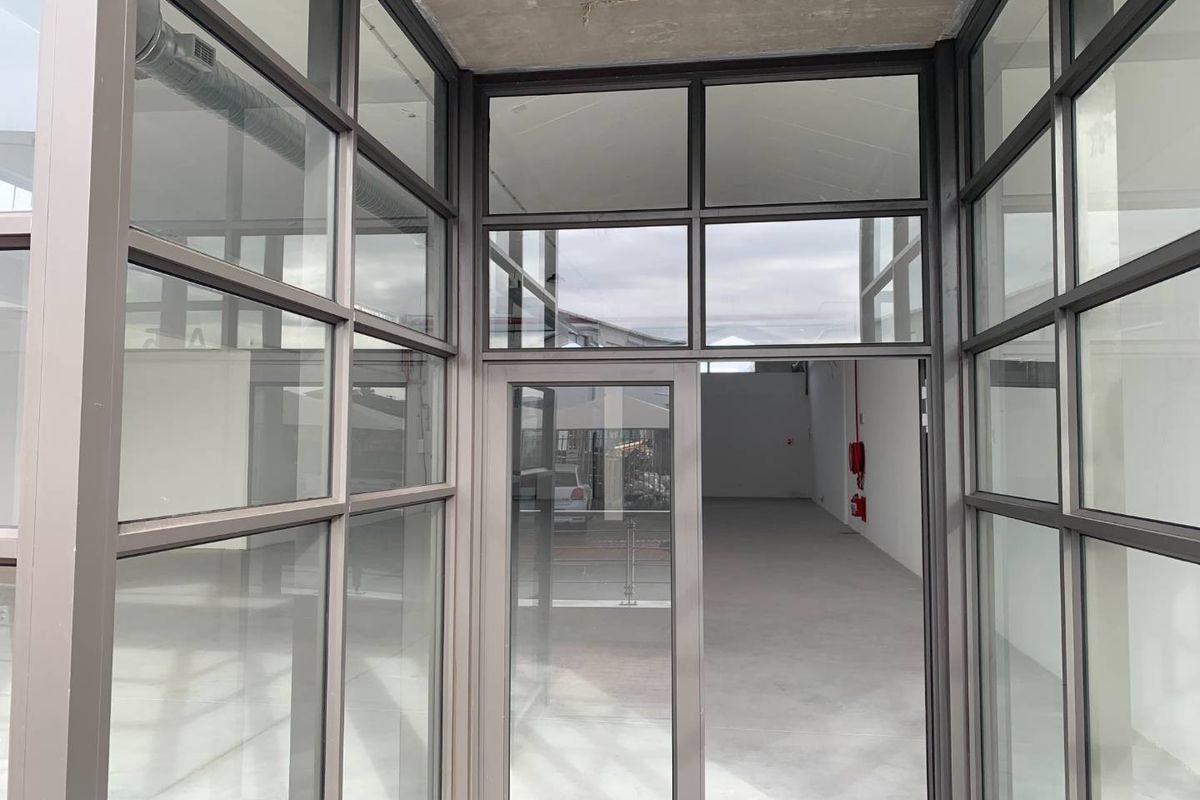 A modern, vacant retail entrance featuring extensive aluminium-framed glass partitioning, polished concrete floors, and an exposed industrial-style ceiling.