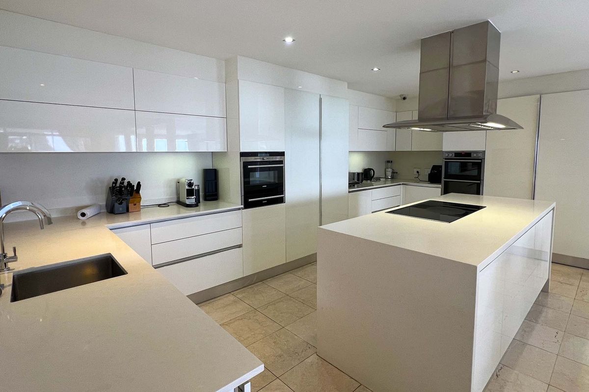 Modern kitchen featuring high-gloss cabinetry, a central island with integrated cooktop, stone countertops, and stainless steel extractor fan.