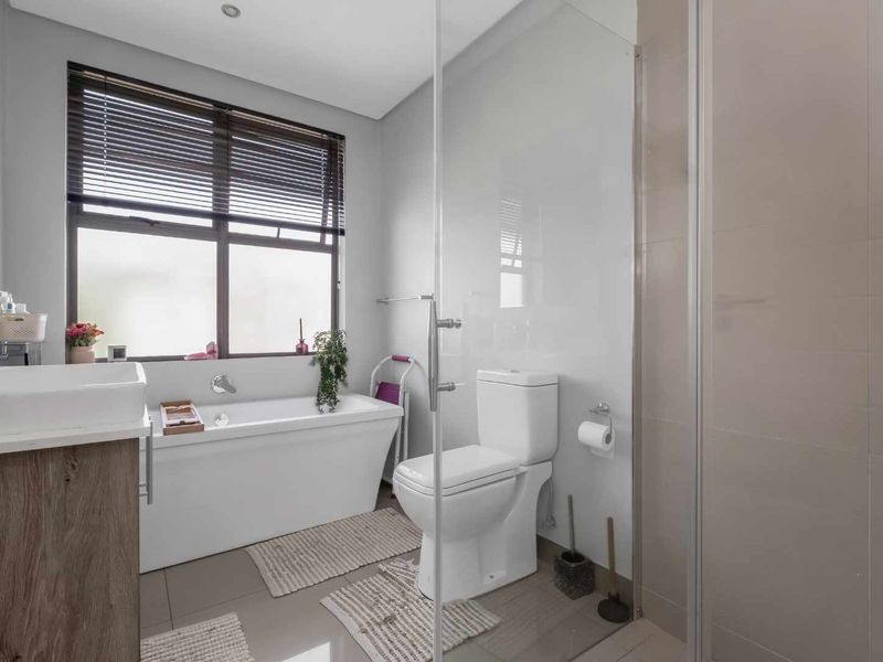 Modern bathroom featuring a freestanding bathtub, glass-enclosed shower, vanity with basin, and neutral tiling, offering a clean and functional space.