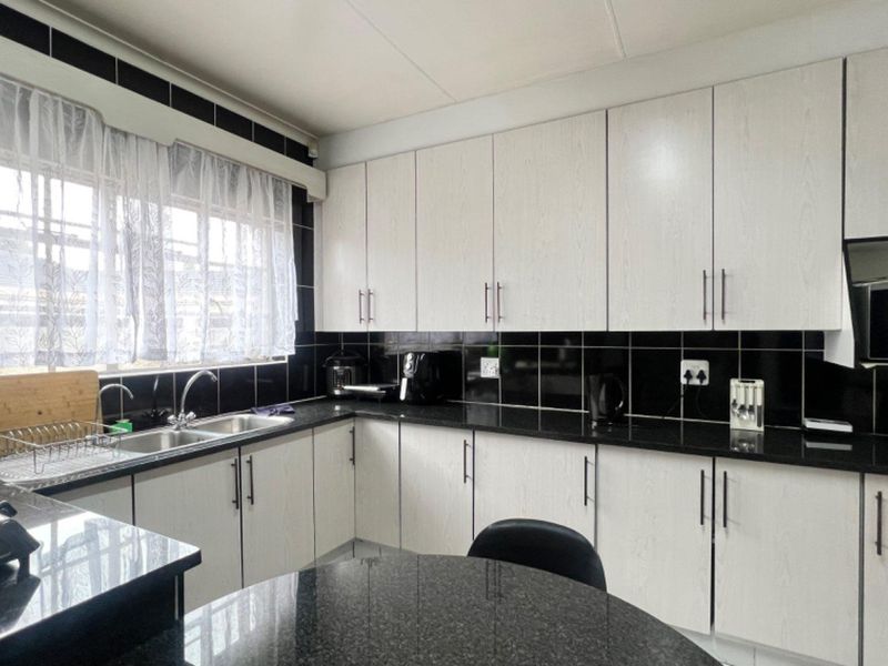 A functional kitchen featuring white cabinetry, black granite countertops, and a contrasting black tiled backsplash with a double basin sink.