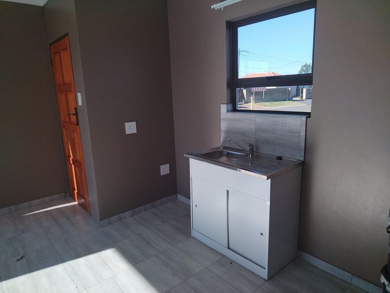 A compact, empty kitchen area featuring a stainless steel sink unit, tiled splashback, tiled flooring, and a timber door.