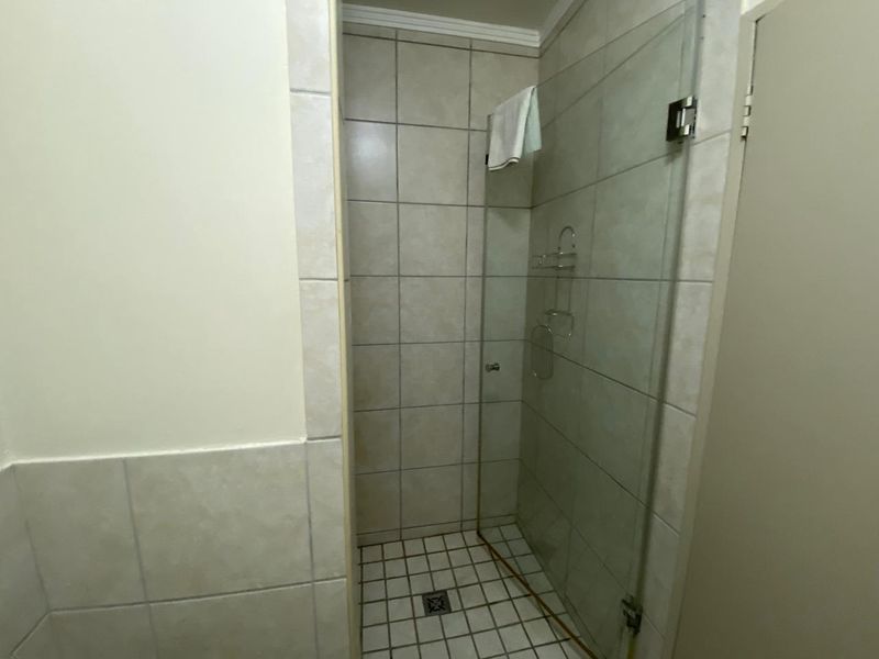 A functional shower enclosure featuring tiled walls, a glass screen, and a floor drain, presenting a clean but dated aesthetic.