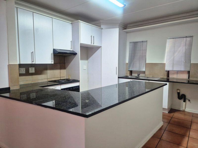 A functional kitchen featuring granite countertops, white cabinetry, a built-in hob with extractor fan, and a double sink with tiled backsplash.
