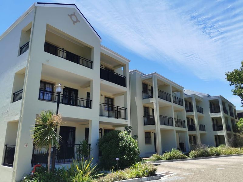 A multi-story apartment building exterior featuring private balconies with metal railings and a paved driveway area.