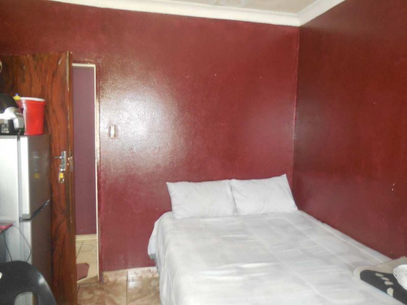 A compact bedroom featuring tiled flooring and dark red painted walls, requiring cosmetic updates to improve the overall aesthetic and finish.